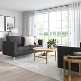 Modernes Wohnzimmer mit großem Fenster, grauem PÄRUP-Sofa, Couchtisch aus Holz und gesprenkeltem Teppich.