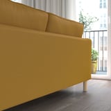 Ein gelbes Sofa mit schlankem Design und abnehmbarem, waschbarem Bezug. Das Licht fällt durch ein großes Fenster, das klare Linien und Holzbeine hervorhebt.