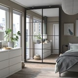 Schlafzimmer ein PAX-Kleiderschrank mit Schiebetüren, weißen Schubladen, einem Bett und Holzboden. Ein Spiegel reflektiert den Raum.