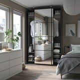 Modernes Schlafzimmer mit PAX-Kleiderschrank aus weißem, laminiertem Holz, mit Glasschiebetüren, organisierten Regalen und verstellbaren Füßen.