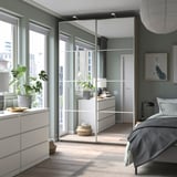 Modernes Schlafzimmer mit PAX-Kleiderschränken mit verspiegelten Schiebetüren, grauer Bettwäsche, weißen Möbeln und Zimmerpflanzen.