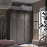 Modernes Schlafzimmer mit dunkelgrauem PAX-Kleiderschrank, hängendem Kleid, Wandkunst, Korbstuhl und großem Fenster.