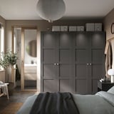 Modernes Schlafzimmer mit dunkelgrauem PAX-Kleiderschrank mit schlankem Design, einschließlich Spiegeln, Aufbewahrungsboxen und einer Hängepflanze zur Dekoration.