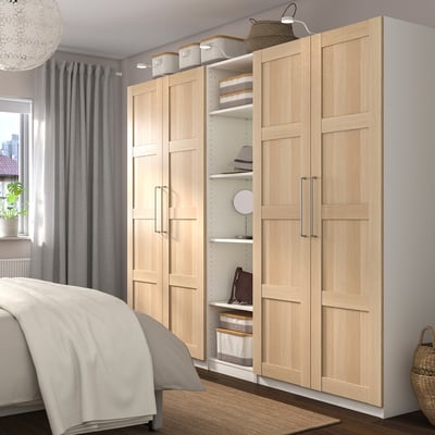 Modernes Schlafzimmer mit großem PAX-Kleiderschrank aus hellem Holz, minimalistischem Dekor, stilvollem Kronleuchter, grauen Vorhängen und gemütlichem Bett.