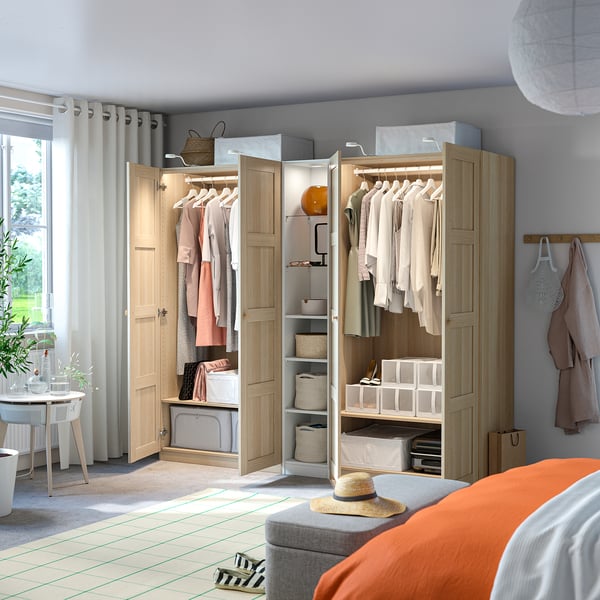 Lichtdurchfluteter Raum mit offenem Holzschrank, PAX, in dem hängende Kleidung ausgestellt ist, Regalen mit gefalteten Kleidern und Aufbewahrungsboxen.