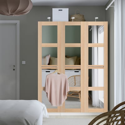 PAX Kleiderschrank in hellem Holzton mit verspiegelten Türen. Hängt ein hellrosa Kleidungsstück auf. Hoch, passt zwischen Tür und Fenster. Modernes, minimalistisches Schlafzimmerdesign.