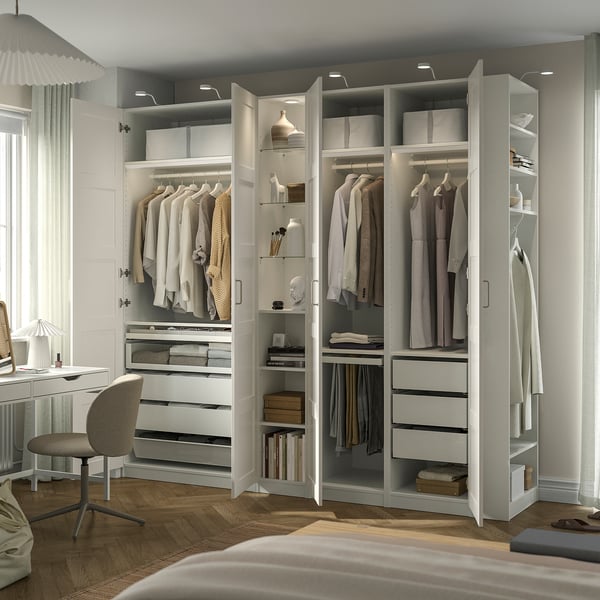 Modernes Schlafzimmer mit PAX-Kleiderschrank , offene Türen, die organisierte Kleidung zeigen. Integrierte Beleuchtung, Schreibtisch und Stuhl in der Nähe.