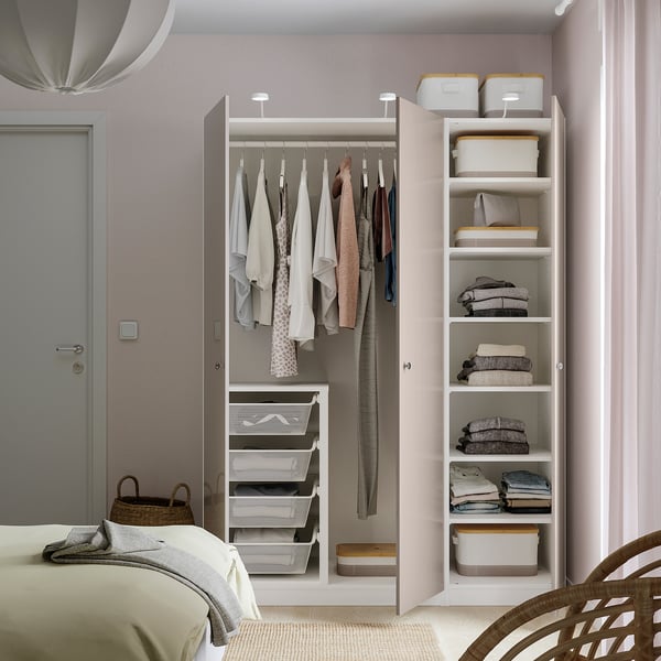 Gepflegtes Schlafzimmer mit weißem PAX-Kleiderschrank. Kleider hängen links, Falten & Schachteln rechts. Wandbefestigung für Stabilität.