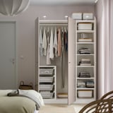 Gepflegtes Schlafzimmer mit weißem PAX-Kleiderschrank. Kleider hängen links, Falten & Schachteln rechts. Wandbefestigung für Stabilität.