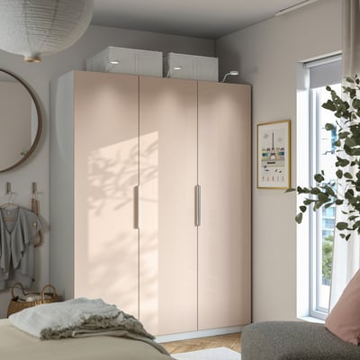 Modernes Schlafzimmer mit großem beigem PAX-Kleiderschrank, grauen Wänden, natürlichem Licht und Pflanzen. Der Kleiderschrank ist hoch und schließt die Schranktüren.