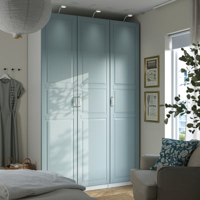 Modernes Schlafzimmer mit hohem hellblauem PAX-Kleiderschrank, grauem Sofa und Pflanze.