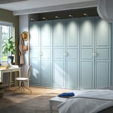 Modernes Schlafzimmer mit großem hellblauem PAX-Kleiderschrank, Schreibtisch, Stuhl und Bett. Der Schrank lässt sich mit Scharnieren sanft schließen und wird von oben beleuchtet.