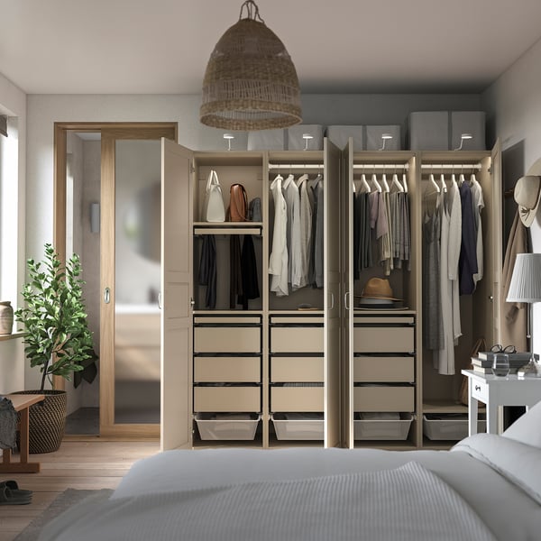 Moderner begehbarer Kleiderschrank mit verspiegelten Schiebetüren, organisierten, beigen Schubladen, hängender Kleidung, offenem Kleiderschrank mit Aufbewahrungsboxen und einer großen Pflanze.