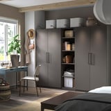 Moderner Schlafzimmer-PAX-Kleiderschrank in Dunkelgrau mit Regalen, einem geflochtenen Stuhl, einem Holzschreibtisch und einem großen Fenster.