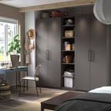 Modernes Schlafzimmer mit grauem PAX-Kleiderschrank, Holzbalken, Schreibtisch und Pflanzen.