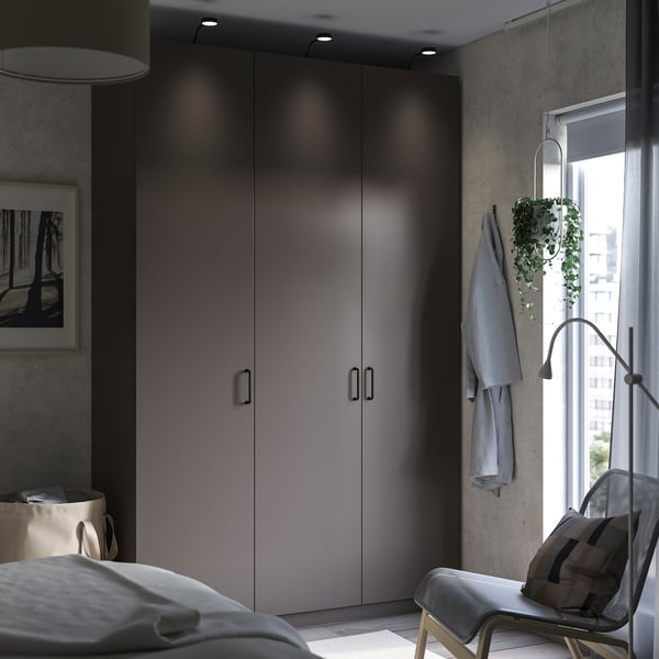 Modernes Schlafzimmer mit PAX-Kleiderschrank, grauem, minimalistischem Design, einem Stuhl und einer Hängepflanze in der Nähe des Fensters.