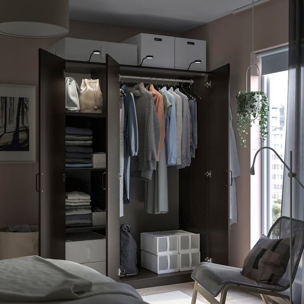 Modernes Schlafzimmer mit schwarzem PAX-Kleiderschrank, Kleidung und Stauraum. Stuhl am Fenster mit Blick auf die Pflanze und die Stadt.