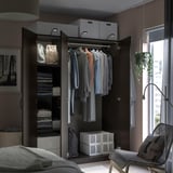 Modernes Schlafzimmer mit schwarzem PAX-Kleiderschrank, Kleidung und Stauraum. Stuhl am Fenster mit Blick auf die Pflanze und die Stadt.
