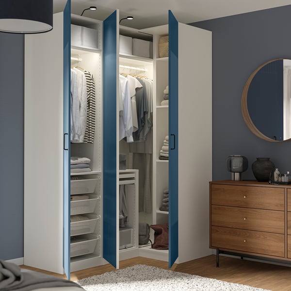 Moderner Kleiderschrank mit blauen Türen, die sich öffnen lassen und ordentlich angeordnete Kleidung, Regale und Aufbewahrungsbehälter präsentieren. Kommode aus Holz mit Spiegel daneben.
