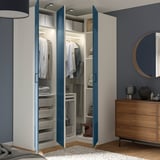 Moderner Kleiderschrank mit blauen Türen, die sich öffnen lassen und ordentlich angeordnete Kleidung, Regale und Aufbewahrungsbehälter präsentieren. Kommode aus Holz mit Spiegel daneben.