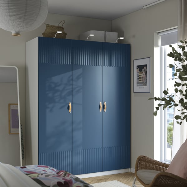 Modernes Schlafzimmer mit großem blauen PAX-Kleiderschrank, Blumenbett, Korbstuhl und Wandkunst.