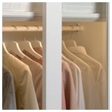 Ein weißer PAX-Schrank mit Schiebetüren und beigen Kleiderbügeln mit heller Kleidung. Die Türen sind oben transparent.