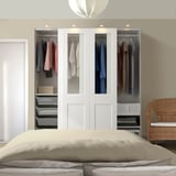 Ein großer weißer PAX-Kleiderschrank neben einem Bett mit mehreren Fächern, in denen Kleidungsstücke ausgestellt sind.