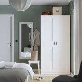 Modernes Schlafzimmer mit weißem PAX-Kleiderschrank. Hohe, schlanke, grüne Wände, klare Linien.