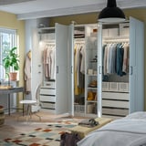 Großer offener Kleiderschrank mit hängender Kleidung, Regalen und Schubladen. Die integrierte Beleuchtung beleuchtet den organisierten Kleiderschrank.