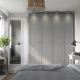Modernes Schlafzimmer mit großem grauen PAX-Kleiderschrank und Soft-Close-Scharnieren. Der Kleiderschrank ragt über das Bett und grenzt an ein minimalistisches Badezimmer mit rahmenlosem Spiegel.