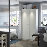 Moderner weißer PAX-Kleiderschrank in kleinem Raum, hoch, schlank, mit oberem Regal und Beleuchtung.