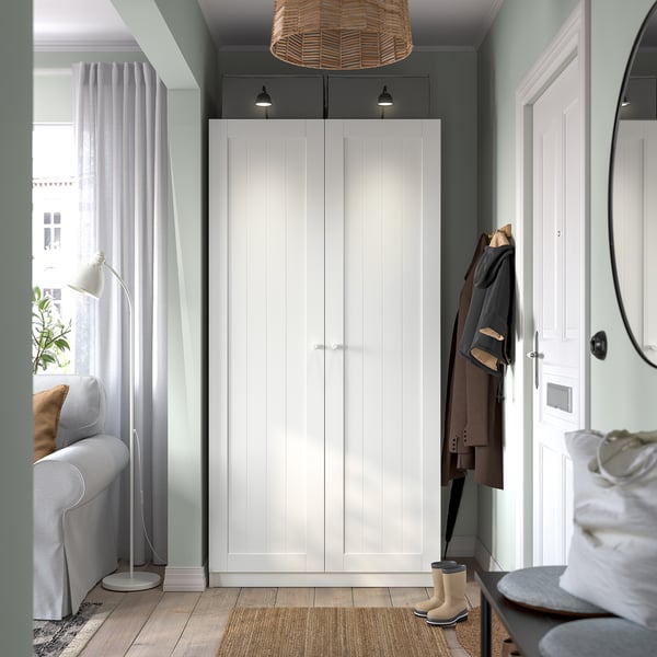 Modernes Zimmer mit großem weißem PAX-Kleiderschrank. Graue Vorhänge, Jacke, Stiefel und Spiegel. Heller Holzboden.