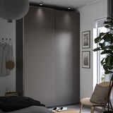 Modernes Schlafzimmer mit grauem PAX-Kleiderschrank, Holzstuhl, Pflanze und Kunstdruck.