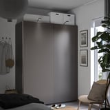 Ein modernes Schlafzimmer mit dunkelgrauem PAX-Kleiderschrank, weißen Boxen, einem Holzstuhl, einer Pflanze und gerahmten Fotos. Ein gemütlicher und organisierter Raum.