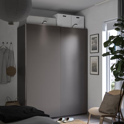 Ein modernes Schlafzimmer mit dunkelgrauem PAX-Kleiderschrank, weißen Boxen, einem Holzstuhl, einer Pflanze und gerahmten Fotos. Ein gemütlicher und organisierter Raum.