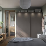 Ein modernes Schlafzimmer mit einem grauen PAX-Kleiderschrank, Schiebetüren und oberen Aufbewahrungsboxen.