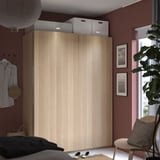 Schlafzimmer mit großem hellbraunen Holzschrank, Schiebetüren und moderner Einrichtung. Pflanze, Kunstwerk und Korbstuhl in der Nähe.