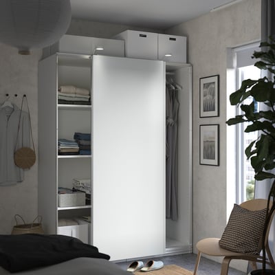 Modernes Schlafzimmer mit weißem PAX-Kleiderschrank, grauer Kleidung, Pflanze, Stuhl, Sandalen und Kunst.