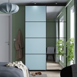 Modernes Schlafzimmer mit blauem PAX-Kleiderschrank, grünen Wänden, Pflanzen und verspiegelten Türen. Weißes Bett, Bademantel, grauer Stuhl und große Pflanze.