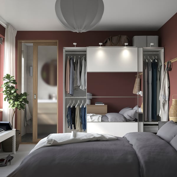 Modernes Schlafzimmer mit weißem PAX-Kleiderschrank, roten Wänden, grauem Bett und Pflanze.