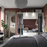 Modernes Schlafzimmer mit weißem PAX-Kleiderschrank, roten Wänden, grauem Bett und Pflanze.
