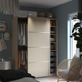 Modernes Schlafzimmer mit einem beigen PAX-Kleiderschrank, Schiebetüren, die sich öffnen lassen und Kleiderbügel und Regale freigeben.