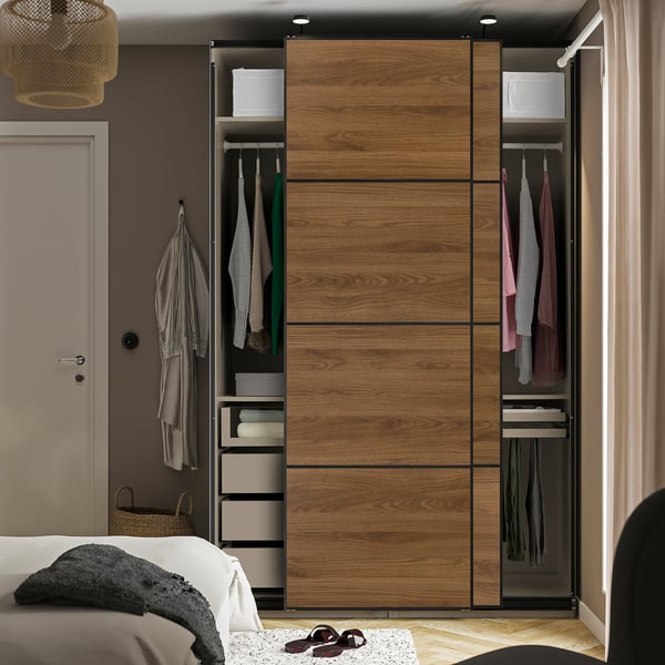 Schlafzimmer mit Holzschiebetürenschrank, hängender Kleidung, Regalen und Schubladen.