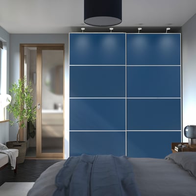Modernes Schlafzimmer, großer blauer PAX-Kleiderschrank . Hoch, überspannte Wand, Schiebetüren, graue Bettwäsche, Holzakzente. Pflanze in der Nähe des Eingangs.