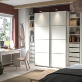 Modernes Schlafzimmer mit PAX-Kleiderschrank mit weißen Schiebetüren, organisierten Regalen und einem beigen Stuhl.
