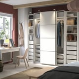 Modernes Schlafzimmer mit weißem PAX-Kleiderschrank, Schiebetüren, Kleidung und Schreibtisch mit Stuhl.