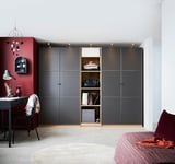 Modernes Schlafzimmer mit großem schwarzen PAX-Kleiderschrank, offenen Regalen mit gefalteter Kleidung und Accessoires. Schreibtisch mit Stuhl, rote Akzente.