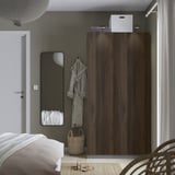 Modernes Schlafzimmer, ein großer dunkelbrauner PAX-Kleiderschrank neben einem Wandspiegel, mit einem weißen Bett und einem geflochtenen Korb darunter.