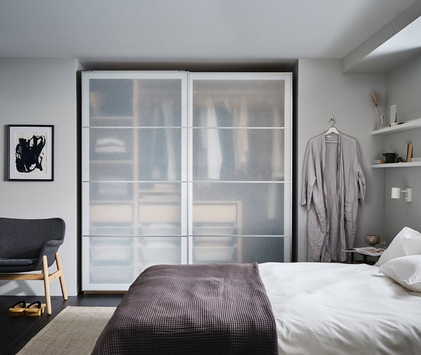 Modernes Schlafzimmer mit grauer Bettwäsche, einem verglasten Kleiderschrank und einem grauen Sessel.