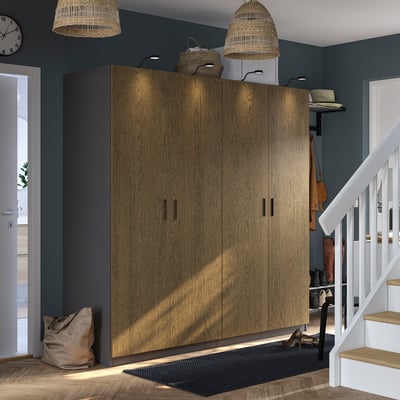 Großer PAX-Kleiderschrank aus Holz im Zimmer, mit grauen Wänden und weißer Treppe, gekrönt mit geflochtenen Körben und stilvollen Lichtern.